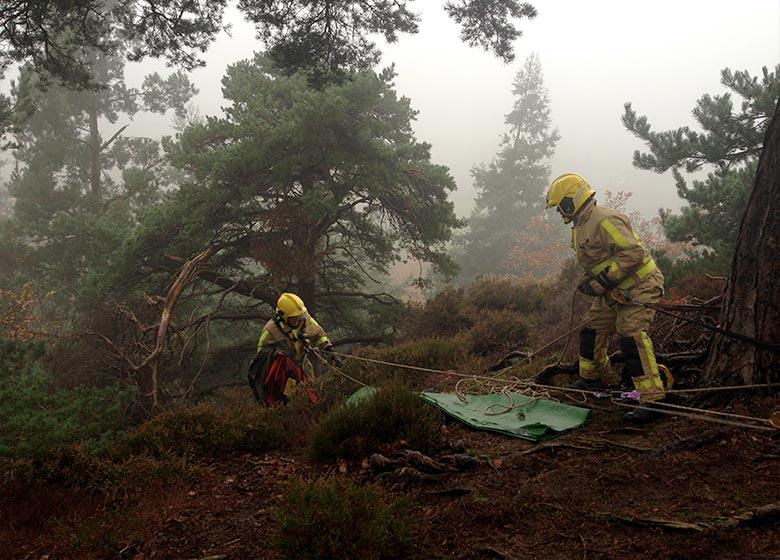 a firefighter starts to descend over the edge of a ledge whilst another guides the rope